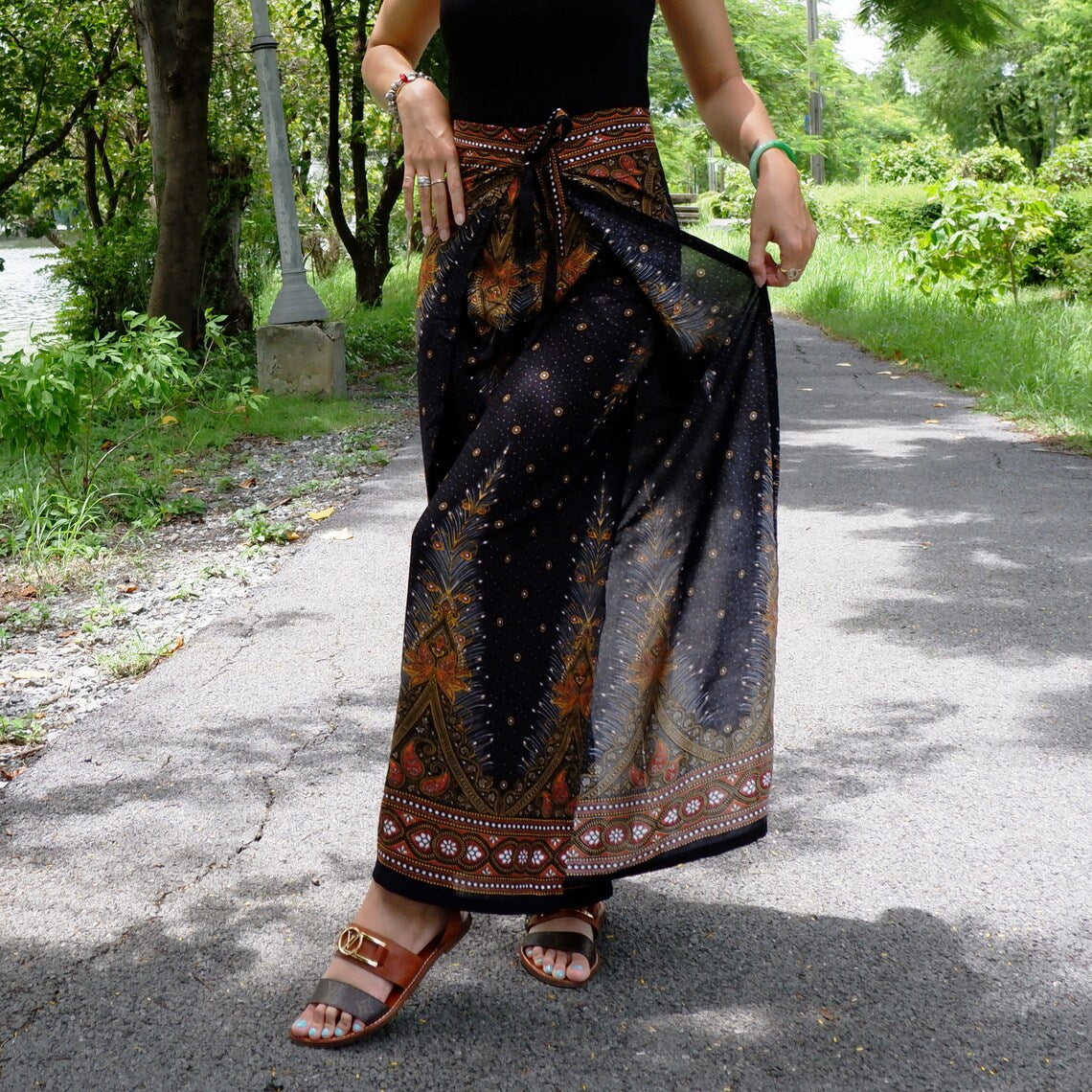 Trendy black boho feather print wrap pants with detailed designs, paired with chic brown sandals, showcased outdoors.