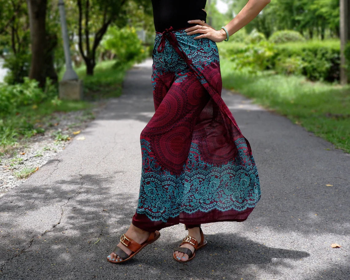 Trendy boho-style beach wrap pants with vibrant red-blue-teal floral design on a garden pathway.