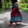 Trendy boho-style beach wrap pants with vibrant red-blue-teal floral design on a garden pathway.