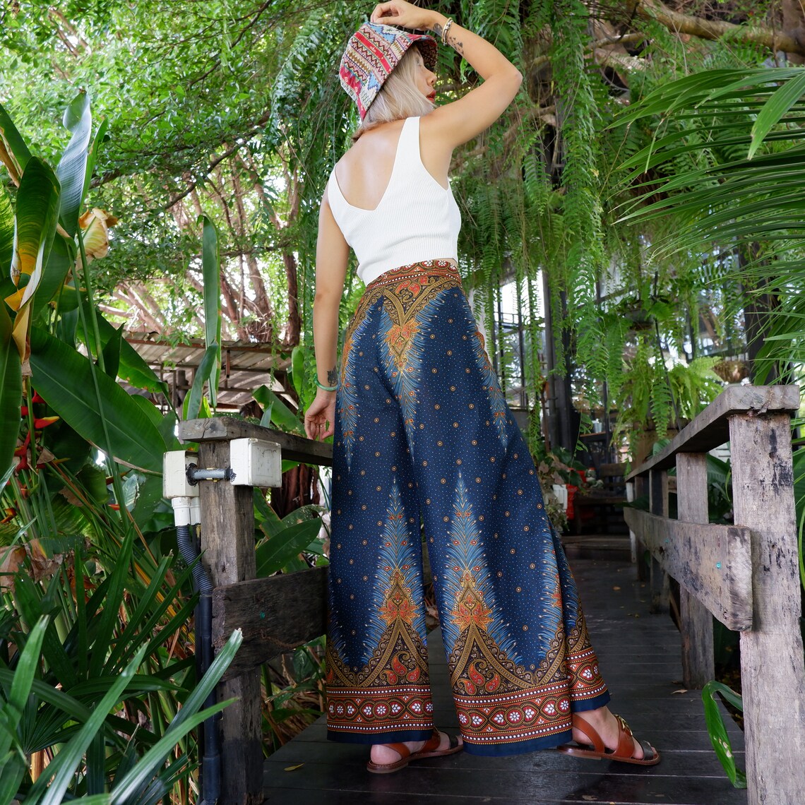 Chic boho feather print wrap pants with a casual white top, showcased on a model standing on a rustic wooden walkway amidst lush greenery.