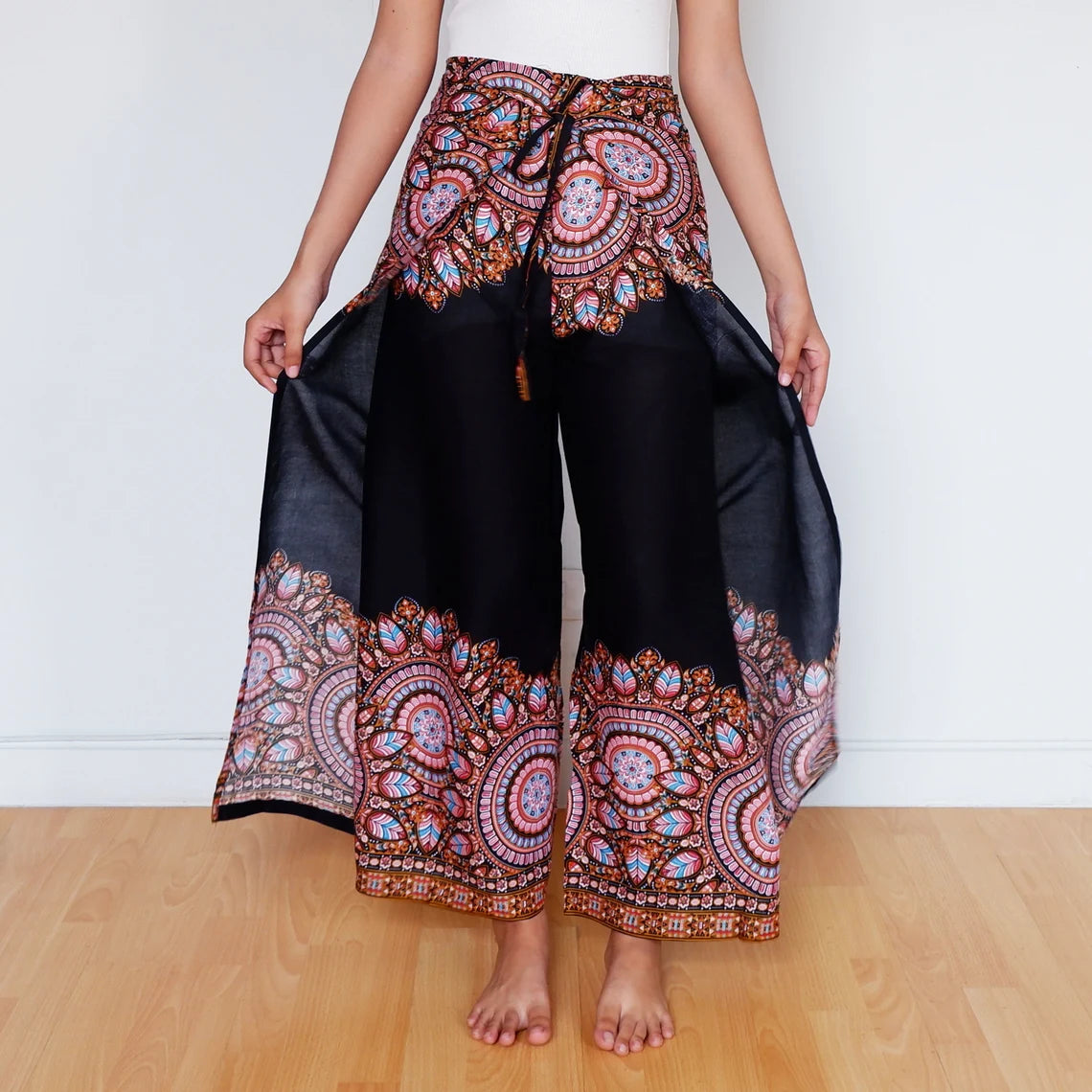 Model fanning out black mandala wrap pants with colorful tribal-style border print.