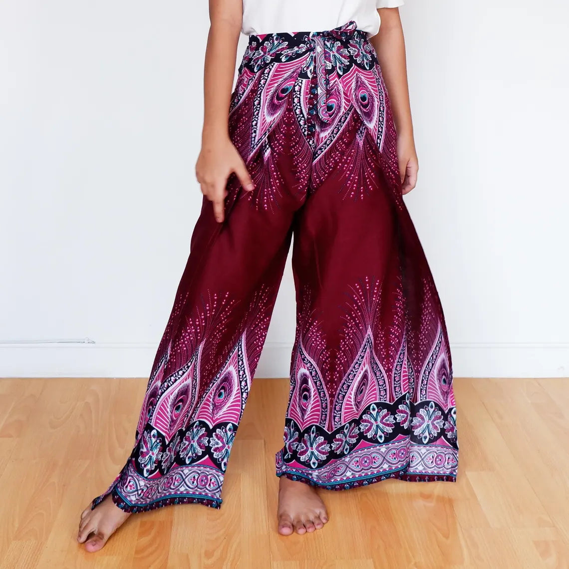 Woman standing in burgundy boho wrap pants featuring feather motifs and floral trim.