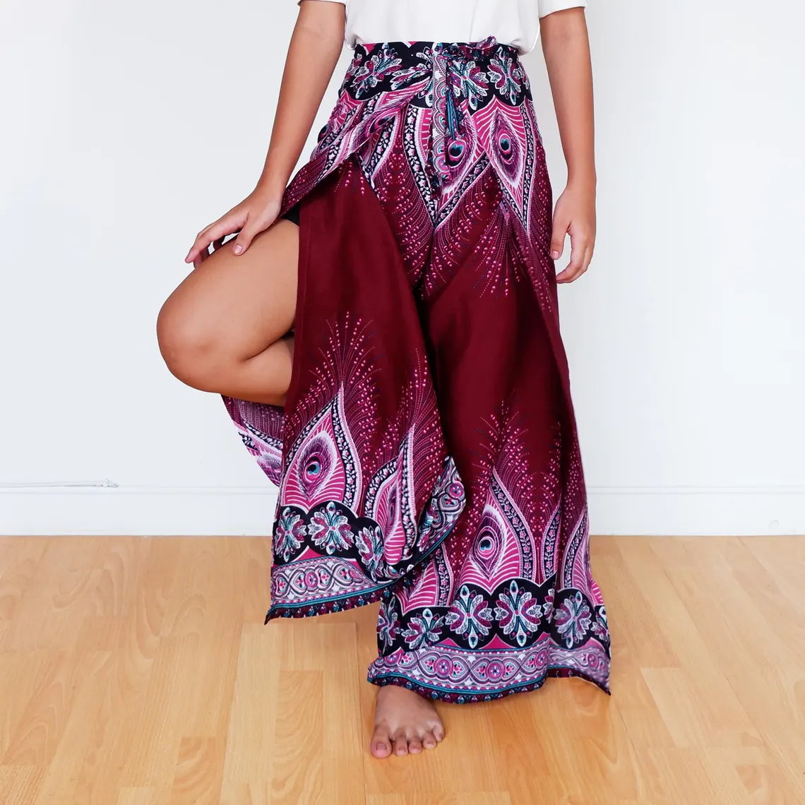 Model lifting leg in burgundy feather print boho wrap pants with tribal floral borders.