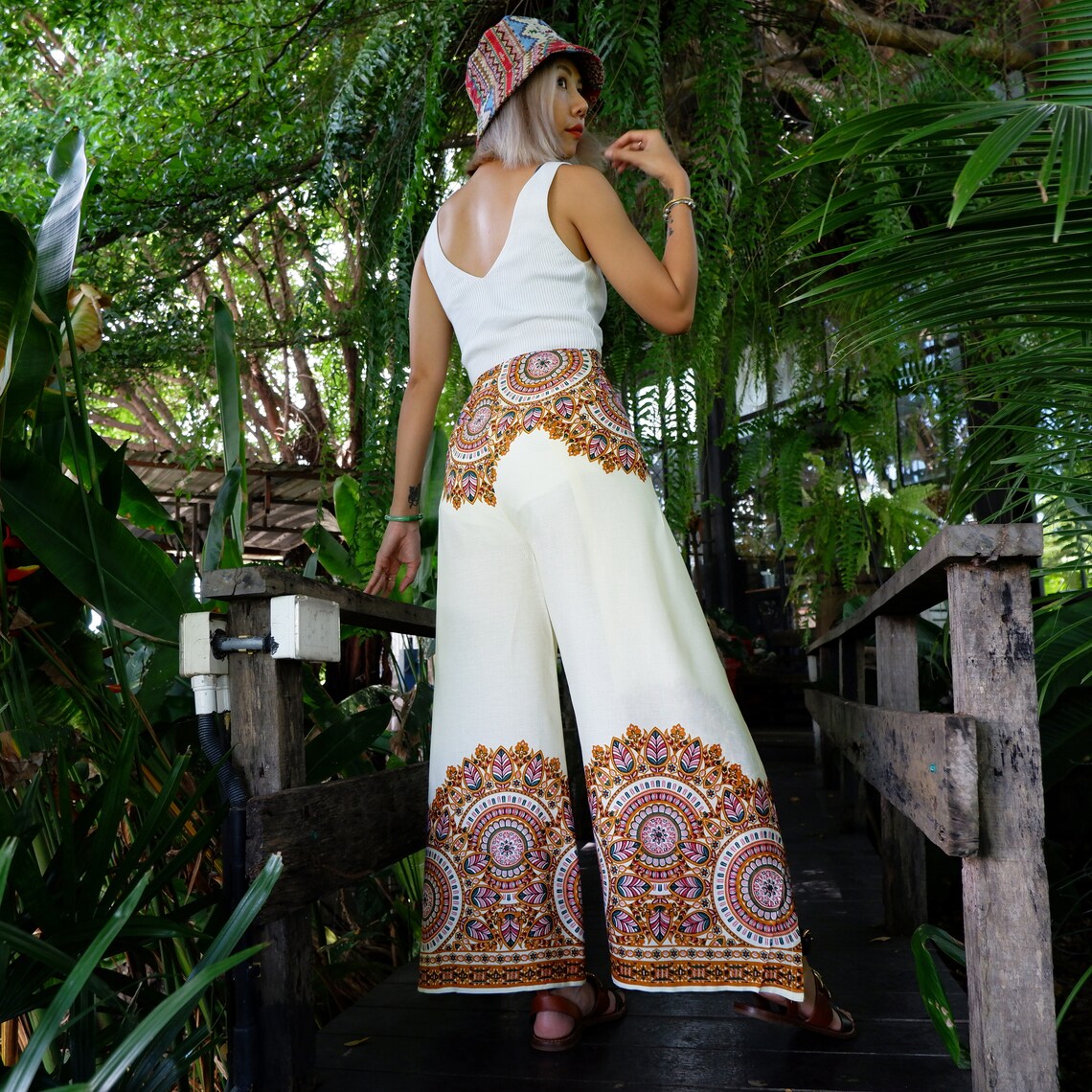 Back view of cream mandala border wrap pants styled with crop top and bucket hat.
