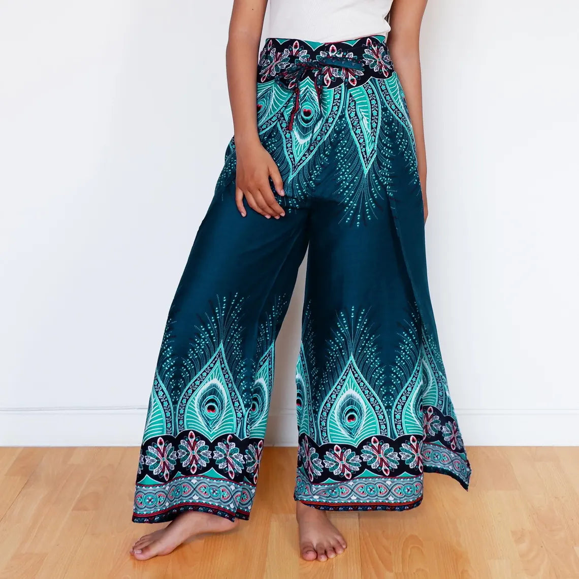 Woman posing in teal boho wrap pants with tribal peacock feather-inspired print.