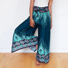 Model lifting leg playfully in teal wrap pants with boho feather and floral design.
