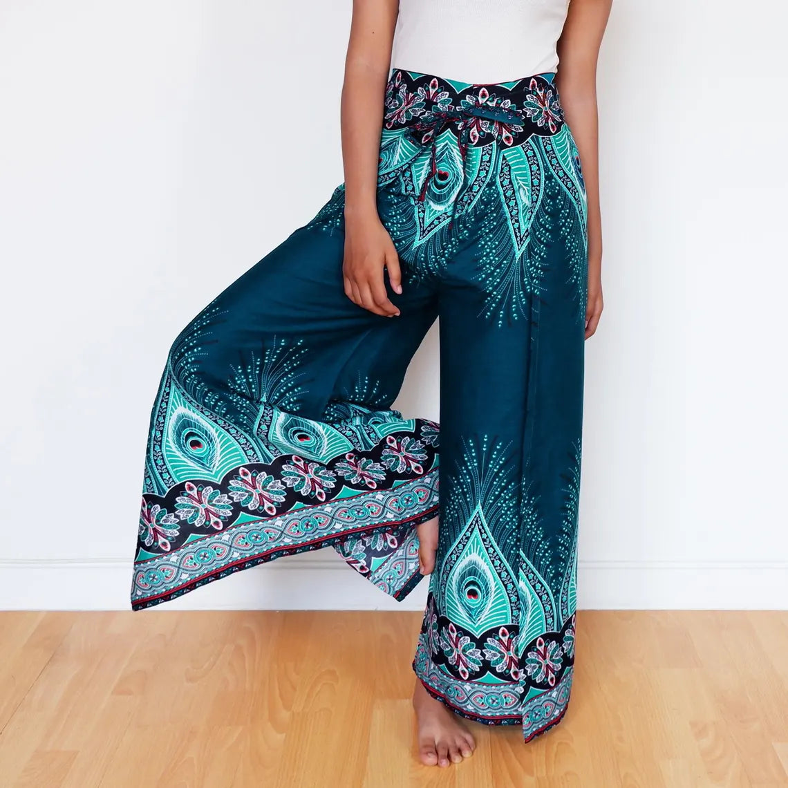Model lifting leg playfully in teal wrap pants with boho feather and floral design.