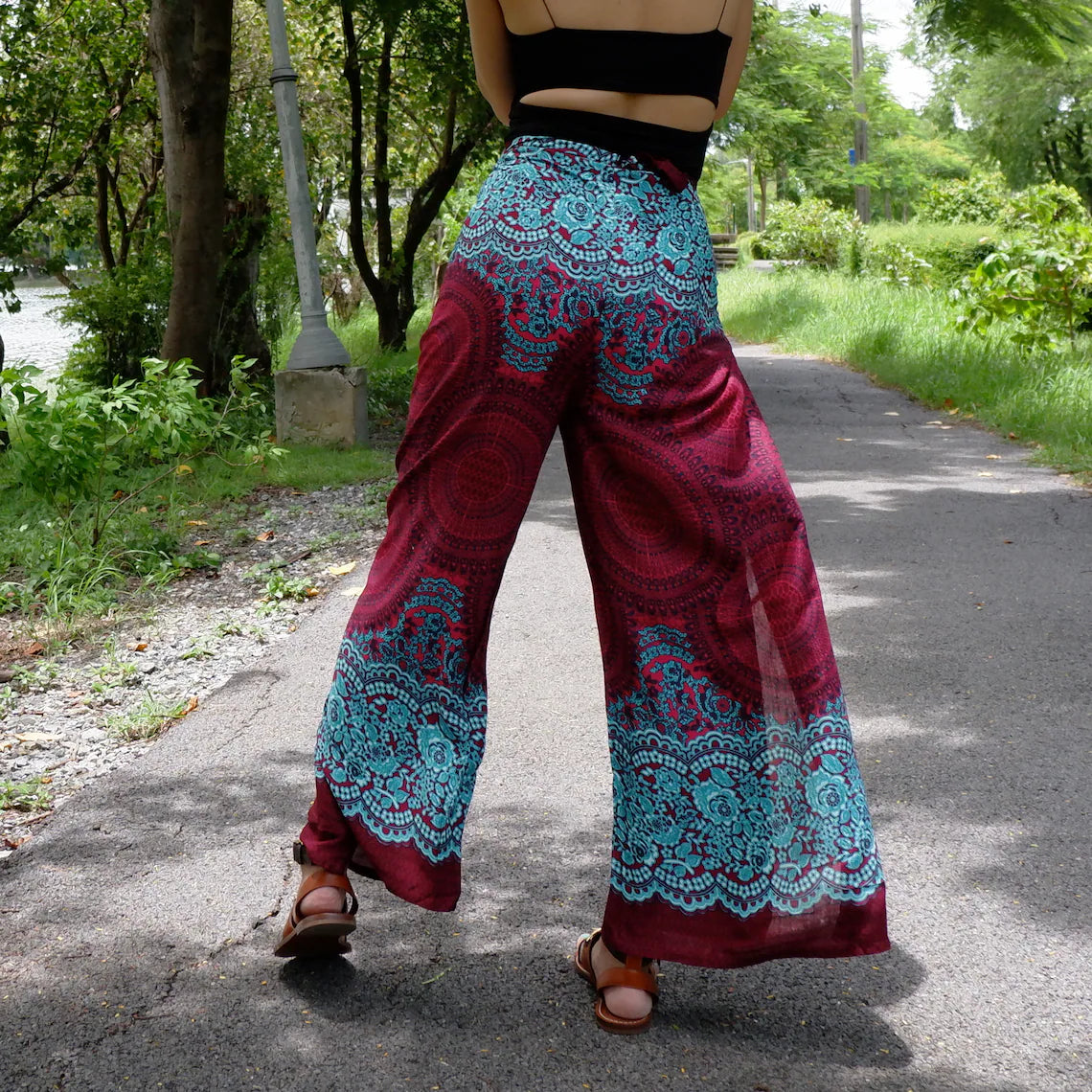 Chic boho-style beach wrap pants with red-turquoise ethnic pattern and brown sandals on a scenic outdoor path.