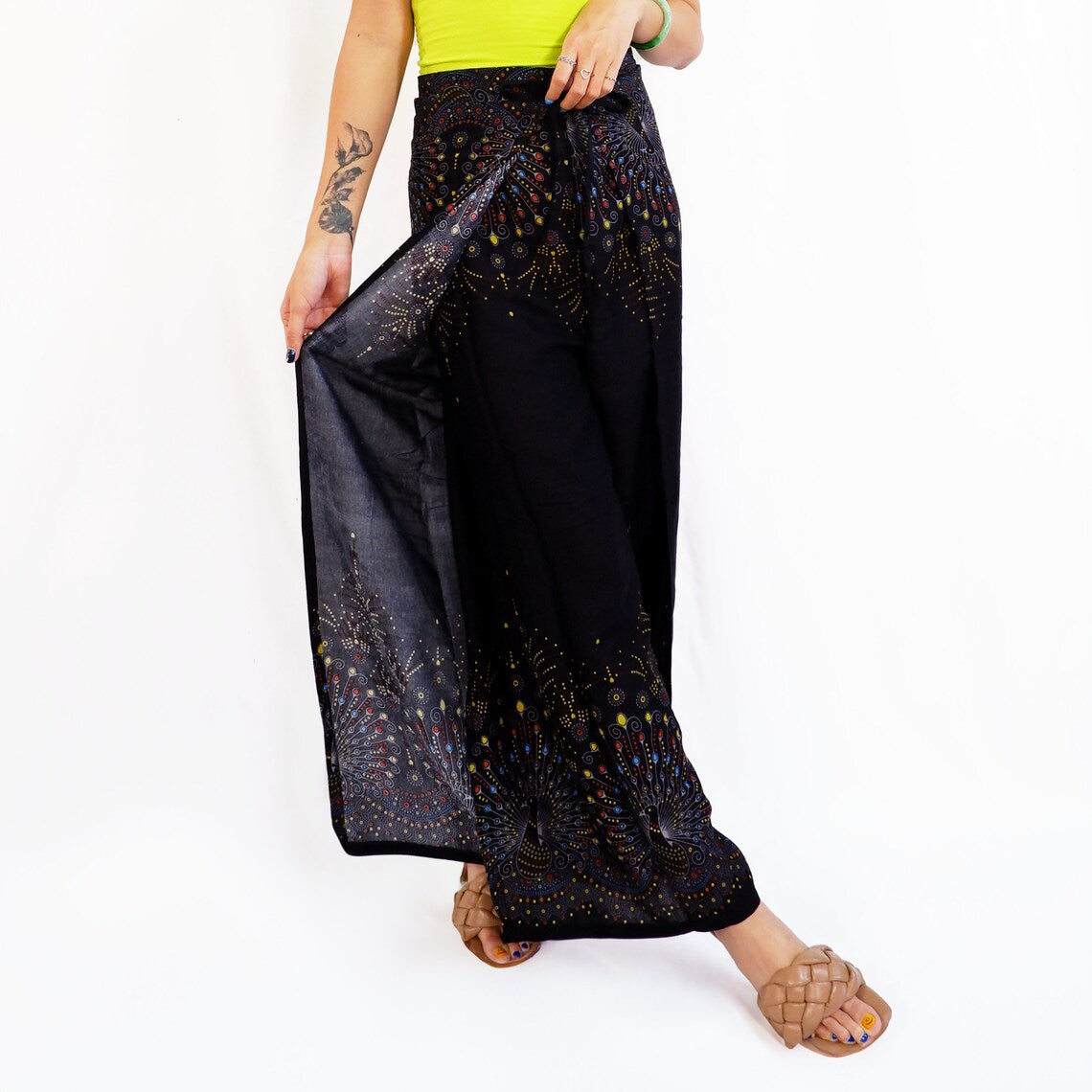 Fashion-forward black boho wrap pants featuring a vibrant peacock print, paired with a green top for a bold statement look.