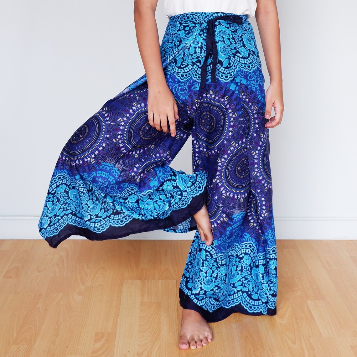 Colorful blue mandala wrap pants with floral print, airy rayon fabric, model lifting leg playfully
