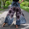 Light mauve and gray festival wrap pants with circular mandala pattern, styled with sandals on a trail
