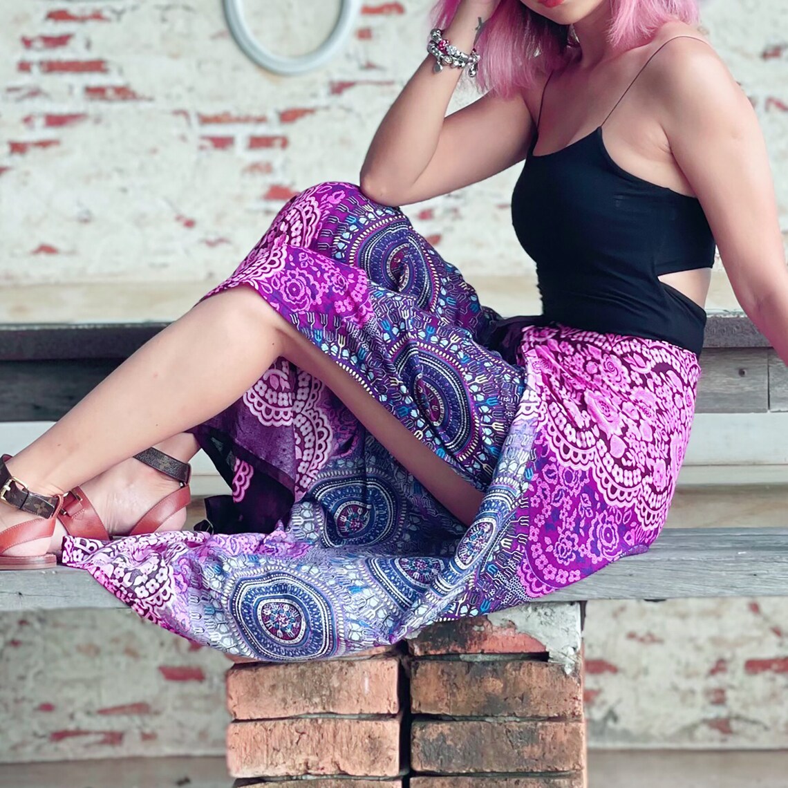 Closeup of wrap pants with pink and purple mandala design, model sitting on bench
