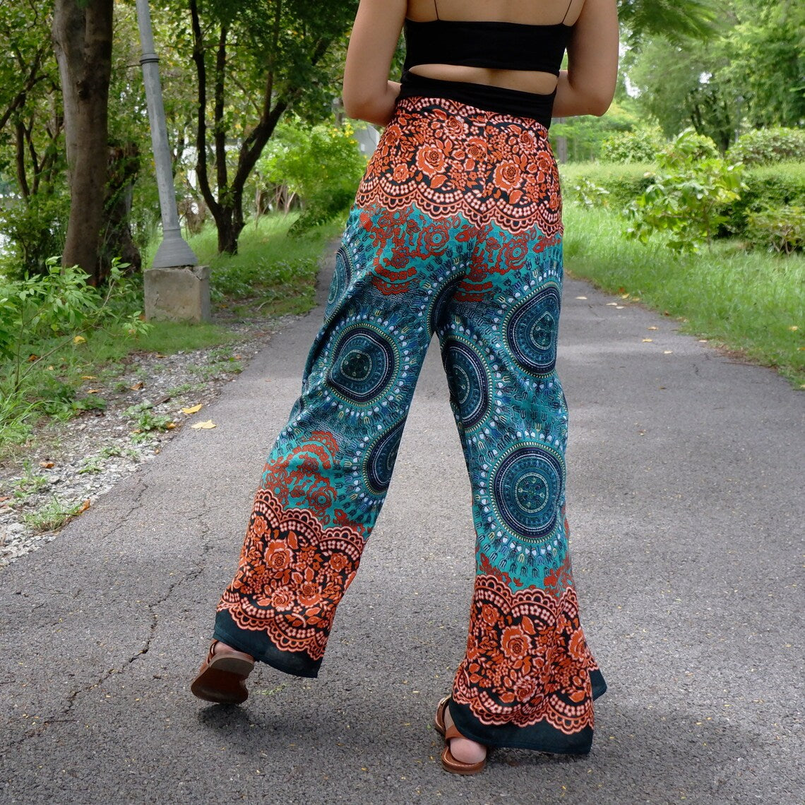 Back view of teal and rust mandala wrap pants with rose floral border, styled with black top outdoors
