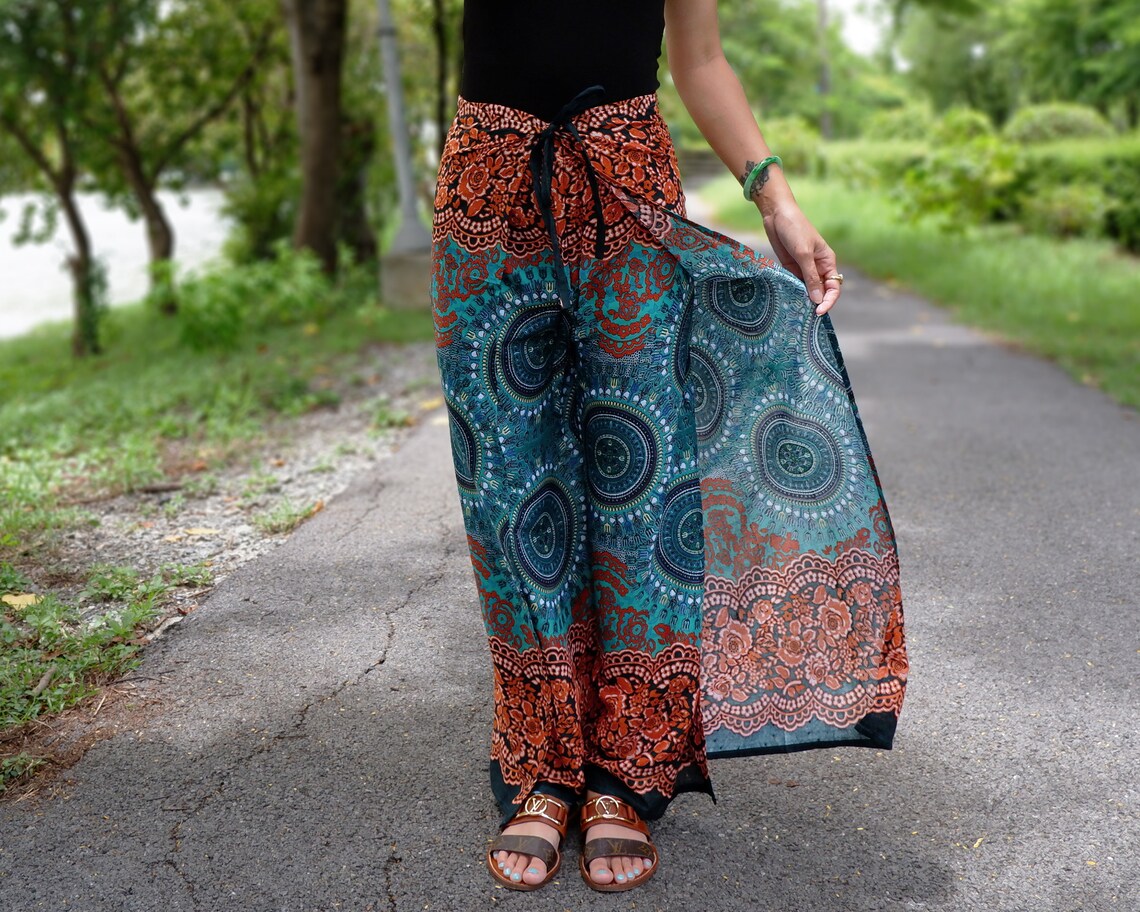 Boho wrap pants in teal and rust with mandala and rose border print, modeled on garden path
