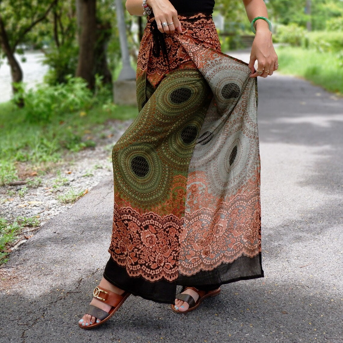 Stylish boho beach wrap pants with green-orange patterns and brown sandals on a garden path.