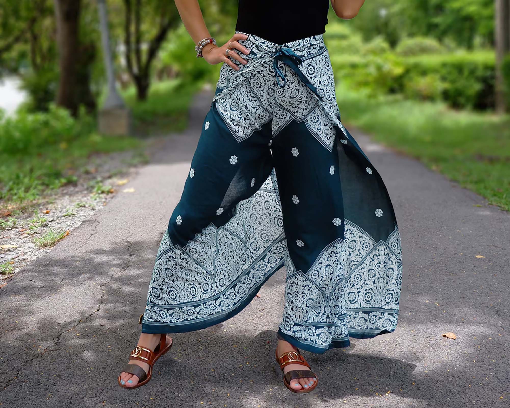 Person in Teal Boho Wrap Pants with Intricate White Floral Pattern on a Paved Pathway Surrounded by Greenery.