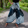 Person in Teal Boho Wrap Pants with Intricate White Floral Pattern on a Paved Pathway Surrounded by Greenery.