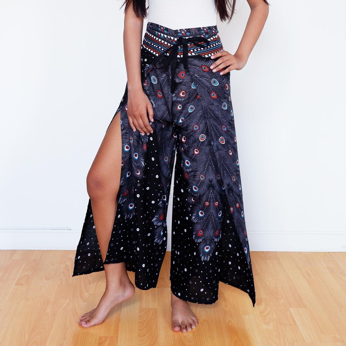 Black wrap pants with bold peacock feather print and leg slit, boho festival vibe
