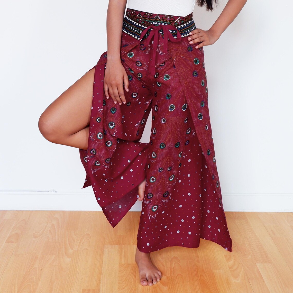 Model lifting maroon wrap pant panel to show wide leg with peacock design
