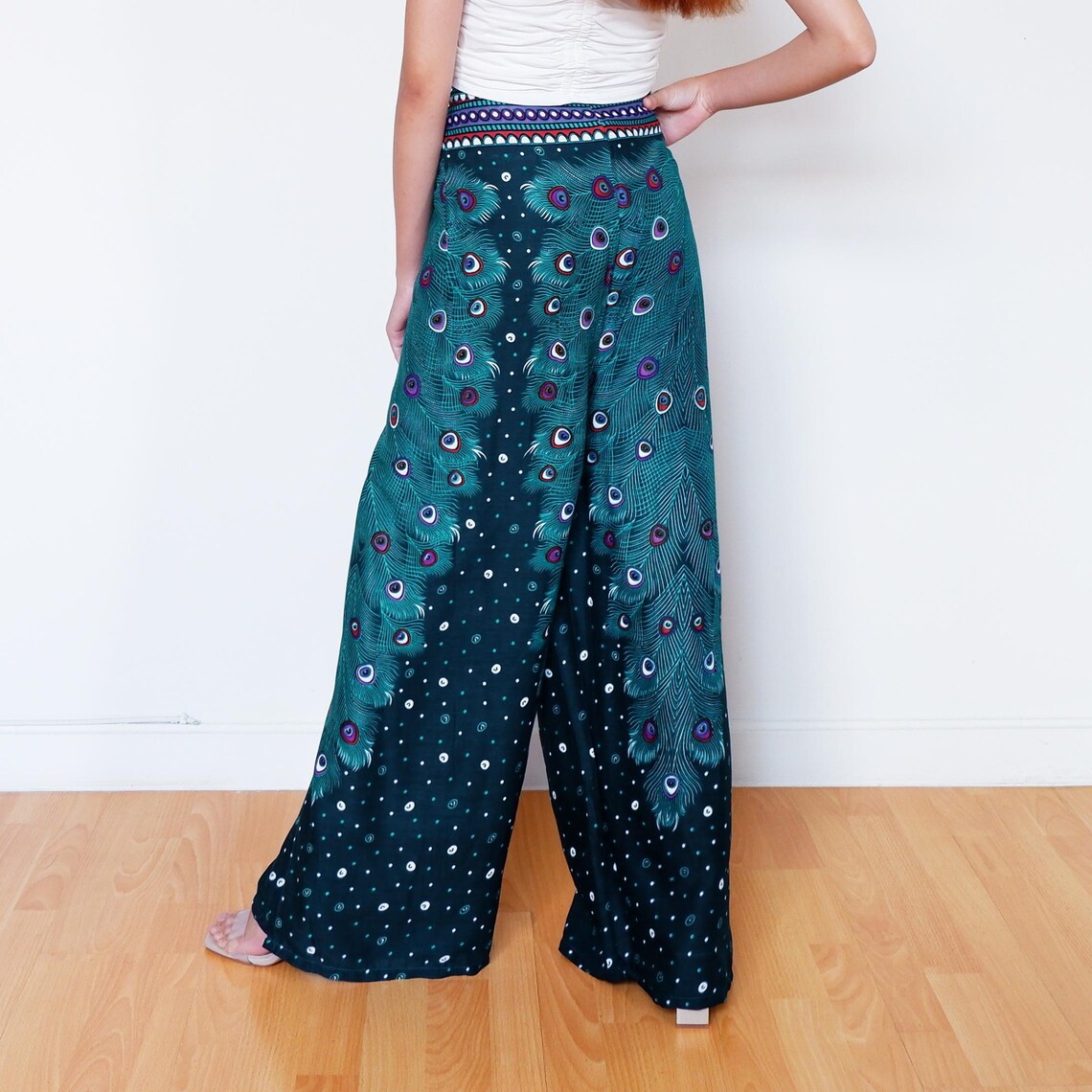 Model wearing teal wrap pants with peacock feather print, shown from the back in boho style
