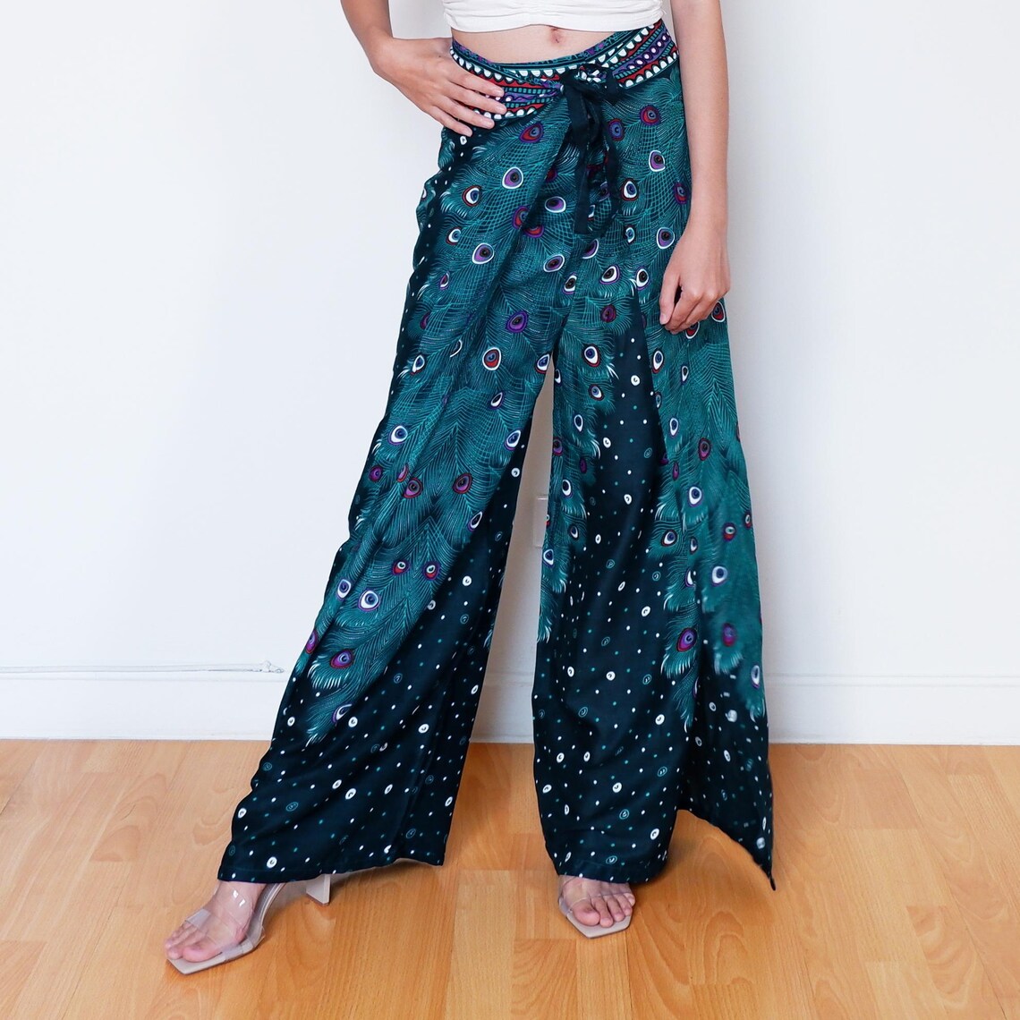 Teal peacock feather wrap pants tied in front, model posing with hand on hip